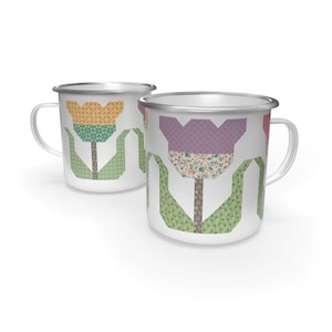 May include: Two white enamel mugs with silver rims and handles. Each mug features a colorful tulip design with a patchwork pattern in shades of yellow, purple, green, and brown. The tulip stems and leaves are green.