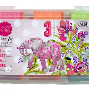 May include: A clear plastic storage case containing 12 spools of Aurifil thread. The spools are arranged in rows and are labelled with the text "Tula Pink Neons & Neutrals Thread Collection". The case also features an illustration of an elephant with floral designs and the text "3 New Colors!"