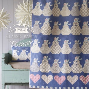 Op de afbeelding: Een blauwe en witte quilt met een patroon van sneeuwpoppen. De quilt is gemaakt met verschillende stoffen en texturen. De quilt wordt getoond op een houten bank met een kussen. De quilt maakt deel uit van de Tilda Classic Basics Collection.