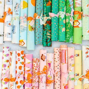 Peut inclure: Collection de rouleaux de tissu noués avec des rubans. Les tissus présentent divers motifs, notamment floraux, fruités et animaliers, dans des couleurs variées comme le vert, le bleu, le rose et le jaune. Les rouleaux sont disposés en rangées.