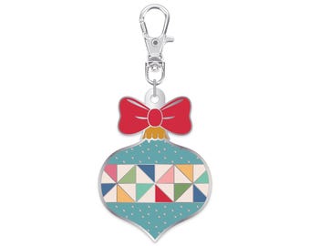 May include: A silver key chain with a red bow and a blue and white patterned ornament. The ornament is shaped like a Christmas tree ornament.