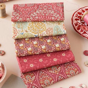 May include: A stack of five fabric squares with floral patterns in shades of pink, red, and cream. The fabrics feature different floral designs, including small flowers, large flowers, and leaves.