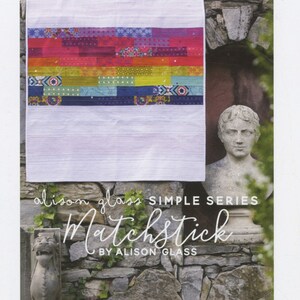 May include: A colorful quilt with a rainbow pattern and the text "alison glass SIMPLE SERIES Matchstick BY ALISON GLASS" is displayed against a stone wall.