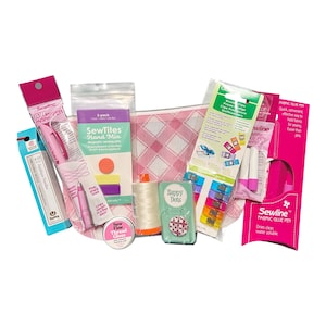 May include: A collection of sewing supplies including a pink fabric pen, a pack of SewTites magnetic pins, a spool of white thread, a small tin of thread gloss, a pack of colourful wonder clips, a fabric glue pen, and a pink plaid zippered pouch.