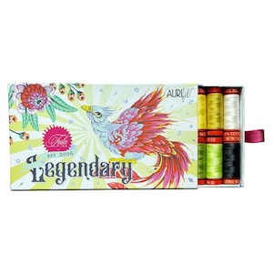 May include: A box set of Aurifil cotton thread spools. The box features a colorful phoenix design with the word "Legendary". The box contains spools of yellow, white, green, and black thread. A pink ribbon is attached to the box.