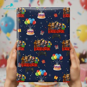 May include: Dark blue wrapping paper featuring a repeating pattern of Roblox characters, birthday cakes, balloons, gift boxes, and game controllers. The word "ROBLOX" is prominently displayed in red. The paper is held by a person.