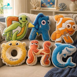 May include: A collection of six plush letter-shaped cushions featuring sea creature designs. The cushions include a green turtle D, a blue fish A, an orange clownfish R, a yellow pufferfish O, an orange octopus H, and a blue shark C, each personalised with a name.