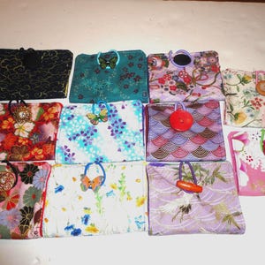 May include: A collection of small, rectangular fabric pouches with various floral and patterned designs. Each pouch features a unique closure, including buttons, beads, and butterfly-shaped accents. The pouches are in shades of red, blue, pink, and green.