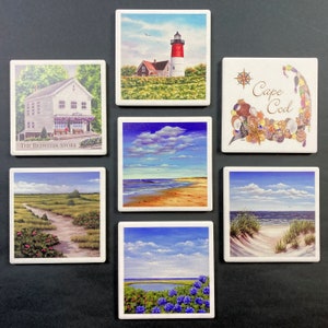 May include: Set of 8 square ceramic coasters featuring various scenes of Cape Cod, including a lighthouse, a beach, a store, and a seashell design with the text "Cape Cod".