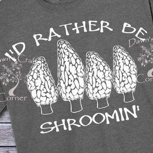 May include: Dark gray t-shirt with the text "I'D RATHER BE SHROOMIN'" in white. The shirt features a graphic of four morel mushrooms. The shirt is made of a soft material and has a crew neck.