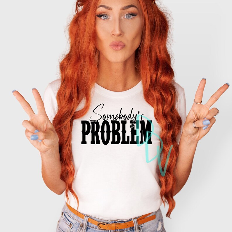 May include: A white t-shirt with the text "Somebody's PROBLEM" in black lettering. The shirt is being worn by a person with long red hair.
