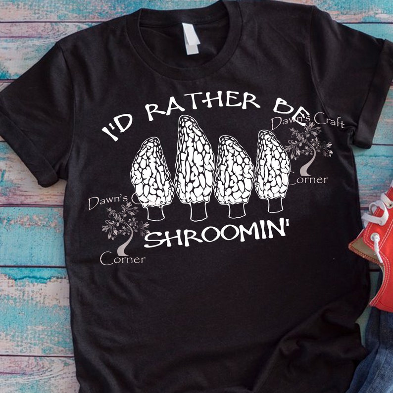 May include: Black t-shirt with a white graphic of four morel mushrooms and the text "I'd Rather Be Shroomin'". The design includes the text "Dawn's Craft Corner".