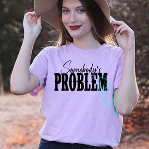 May include: A light purple t-shirt with the text "Somebody's PROBLEM" in black lettering.