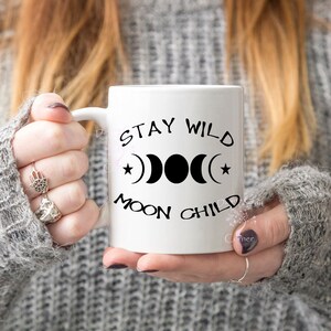 Puede incluir: Taza de cer&aacute;mica blanca con texto negro y un s&iacute;mbolo de fase lunar. El texto dice "Stay Wild Moon Child".