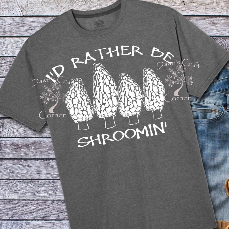 May include: Dark gray t-shirt with the text "I'D RATHER BE SHROOMIN'" in white. The shirt features a graphic of four morel mushrooms. The shirt is made of a soft material and has a crew neck.