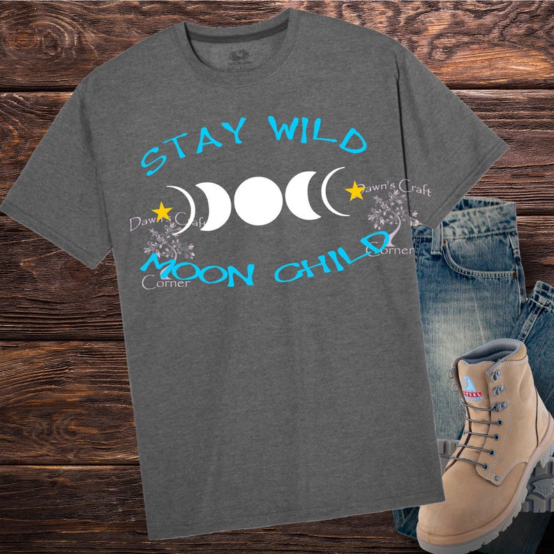 Puede incluir: Una camiseta gris con el texto "Stay Wild Moon Child" en azul y amarillo. El dise&ntilde;o incluye tres lunas y estrellas.