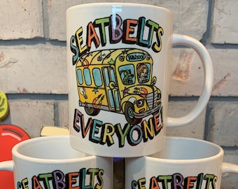 May include: Three white ceramic mugs with a yellow school bus graphic and the text "Seatbelts Everyone" in rainbow colors.