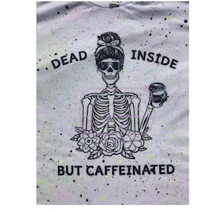 May include: A white t-shirt with a black and white skeleton graphic holding a coffee cup. The skeleton has a messy bun and sunglasses. The text "Dead Inside But Caffeinated" is printed on the shirt in black and yellow.