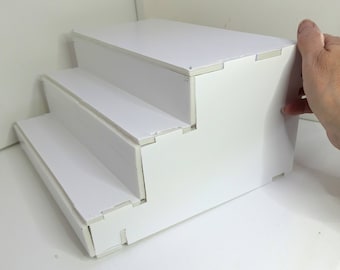 May include: White three-tiered shelf unit made of foam board. The shelf unit is assembled and ready to use.