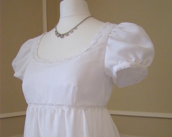 Puede incluir: Un vestido blanco de talle imperio con ribete de encaje y mangas abullonadas. El vestido está hecho de una tela ligera y tiene un diseño simple y elegante.