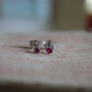 May include: A pair of silver stud earrings with small, round, dark pink gemstones.