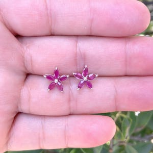 May include: A pair of silver flower-shaped earrings with pink gemstones.