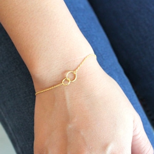 May include: A gold chain bracelet with two interlocking circles. The bracelet is on a person's wrist.