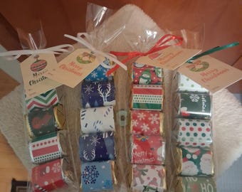 May include: Several small, wrapped chocolate bars arranged in clear cellophane bags, each tied with a ribbon and a tag that says "Merry Christmas." The wrappers feature festive patterns and holiday designs in red, green, and blue.
