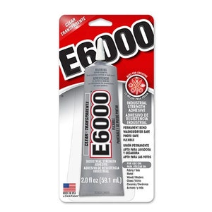 May include: A silver tube of E6000 industrial strength adhesive in clear, transparent formula. The packaging is red and white with black text, featuring a white nozzle cap. The label indicates a volume of 2.0 fl oz and lists uses for fabric, metal, wood, glass, and ceramic.