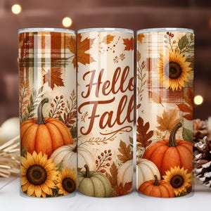 May include: A cylindrical tumbler featuring a fall-themed design with orange pumpkins, yellow sunflowers, and brown autumn leaves against a plaid background. The center displays the text Hello Fall in a brown script font on a cream-colored base.