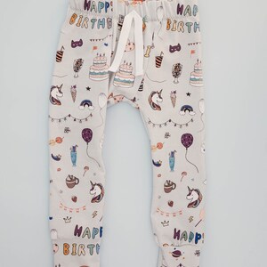 May include: Grey baby leggings with a colourful print of unicorns, balloons, cake, and the words "Happy Birthday".