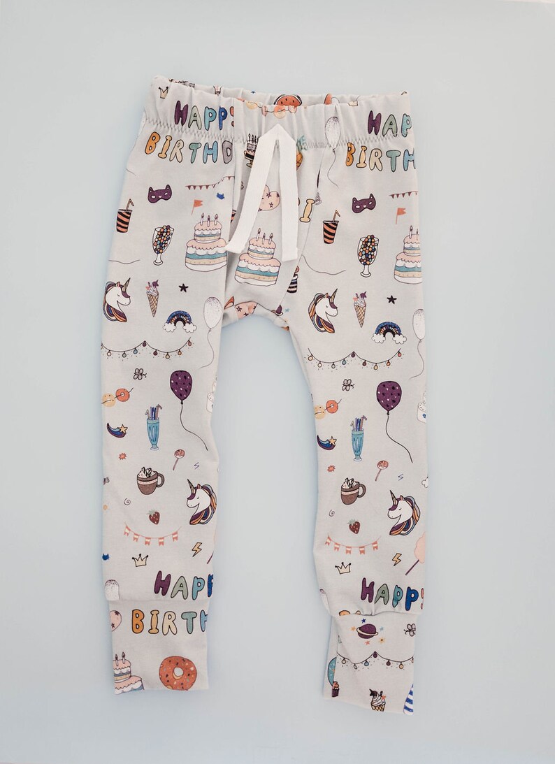 May include: Grey baby leggings with a colourful print of unicorns, balloons, cake, and the words "Happy Birthday".