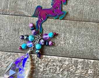 Può includere: Un ciondolo a forma di unicorno arcobaleno iridescente con un prisma di cristallo appeso a una catena d'argento. Il ciondolo è decorato con perline colorate.