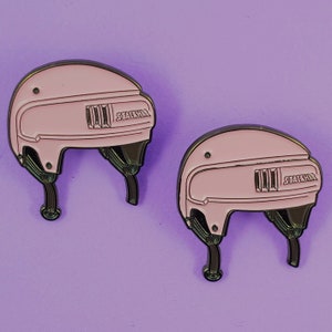 May include: Two pink hockey helmets with black accents and the word "Stackhat" printed on the side.