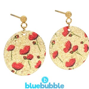 May include: A pair of gold earrings with a round, textured, gold-coloured base and a red poppy floral pattern. The earrings have a gold hook fastening.