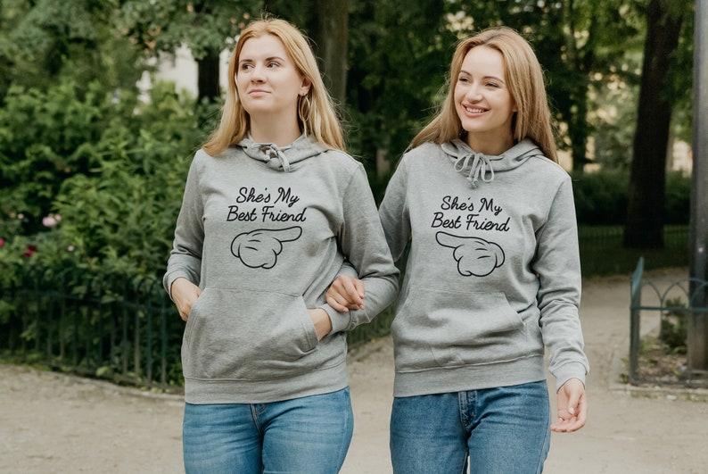 Two women with matching printed hoodies - hoodies with print phrase she is my best friend - herringbone neck tape hoodie - kangaroo pocket, side seams, brushed inside, elastic cuffs and waistband hoodies - grey bff matching hoodies - bestie hoodies