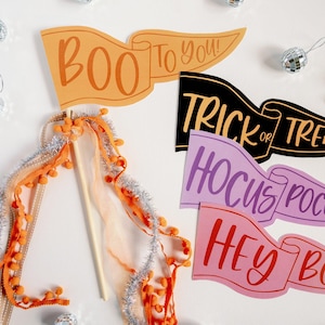May include: Halloween-themed pennant banners with phrases like "Boo to You!" and "Trick or Treat" in orange, black, and pink. Decorative wand with orange pom-poms and silver tinsel. Small disco ball ornaments.