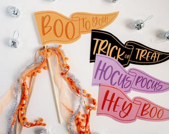 Puede incluir: Banderines de banderín con temática de Halloween con frases como "Boo to You!" y "Trick or Treat" en naranja, negro y rosa. Varita decorativa con pompones naranjas y oropel plateado. Pequeños adornos de bola de discoteca.