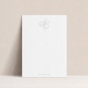 May include: A white card with a simple, elegant script monogram of the letters "ER" in gray. The text "The ______ Family" is printed at the bottom of the card.