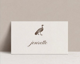 Puede incluir: Una tarjeta de lugar blanca con una ilustración marrón de un pavo y el nombre "jenrette" escrito en cursiva.