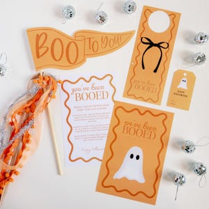 May include: A set of printable Halloween party decorations featuring a ghost and the text "You've been Booed!" in orange and white. The decorations include a door hanger, a sign, and a tag.