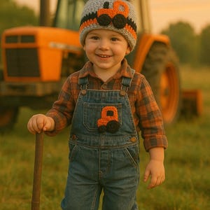 May include: A young child wearing a gray and orange knit hat with a black pom-pom and a tractor design. The child is also wearing a blue denim overall with a matching tractor patch and a plaid shirt. The child is holding a small shovel and standing in a field of grass.