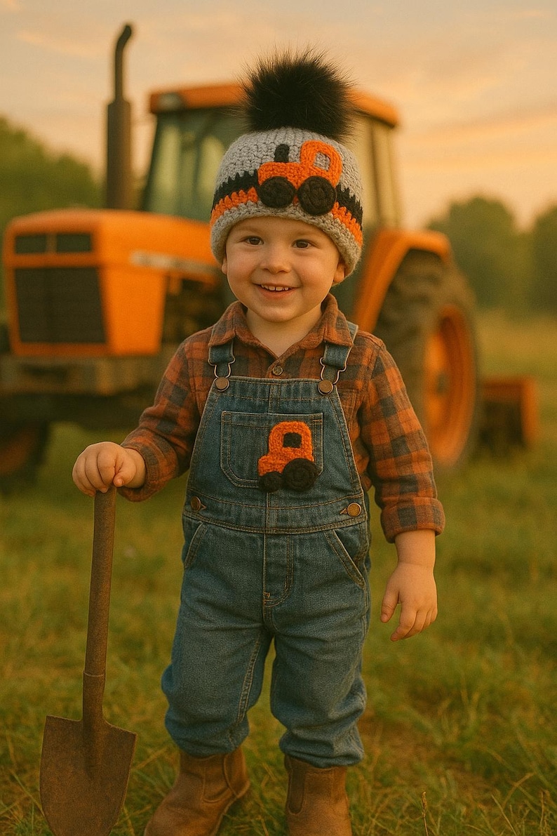 May include: A young child wearing a gray and orange knit hat with a black pom-pom and a tractor design. The child is also wearing a blue denim overall with a matching tractor patch and a plaid shirt. The child is holding a small shovel and standing in a field of grass.