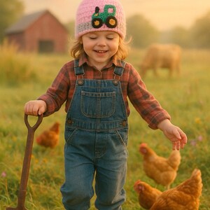 May include: A young child wearing a pink and gray knit hat with a green tractor design and a red plaid shirt walks through a field with a small shovel. The child is smiling and looking down at the ground. There are chickens in the background.