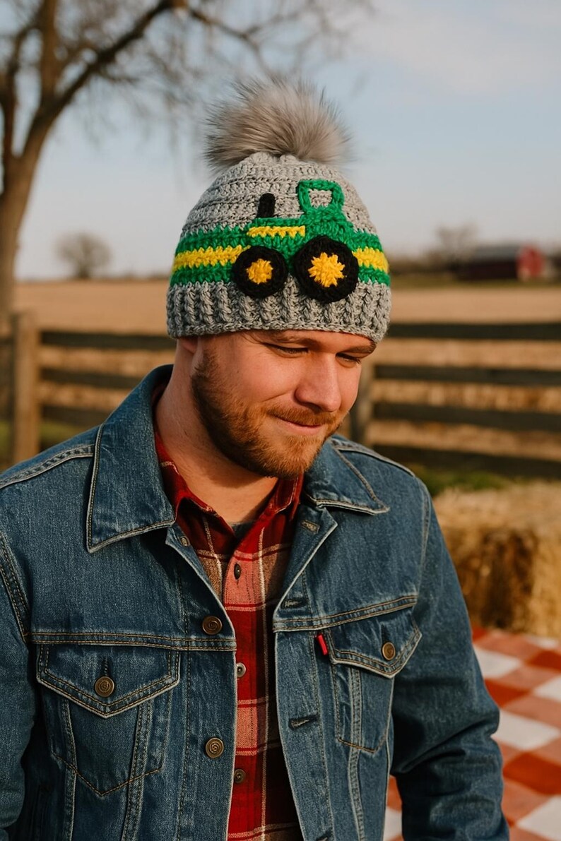 May include: A gray crocheted beanie with a green and yellow tractor design and a faux fur pom pom on top.
