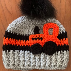 May include: Gray crocheted hat with a black pom pom and an orange and black crocheted tractor design.