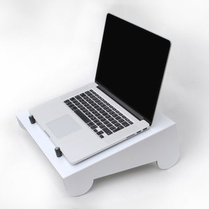 May include: A white laptop stand with a laptop on top. The laptop is silver and has a black screen. The stand is angled and has rounded edges.