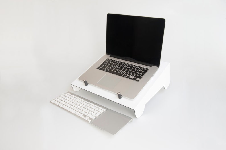 May include: A white laptop stand with a laptop on top of it. The laptop has a black screen and a silver keyboard. A white wireless keyboard with a silver trackpad is in front of the stand.
