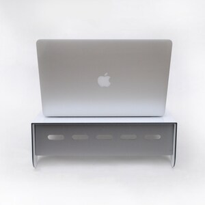 May include: A white laptop stand with a silver laptop on top. The stand has a series of small holes in the front.