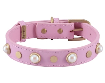 May include: A pink leather dog collar with gold accents and pearl embellishments. The collar has the text "Dosha dog" embossed on it.
